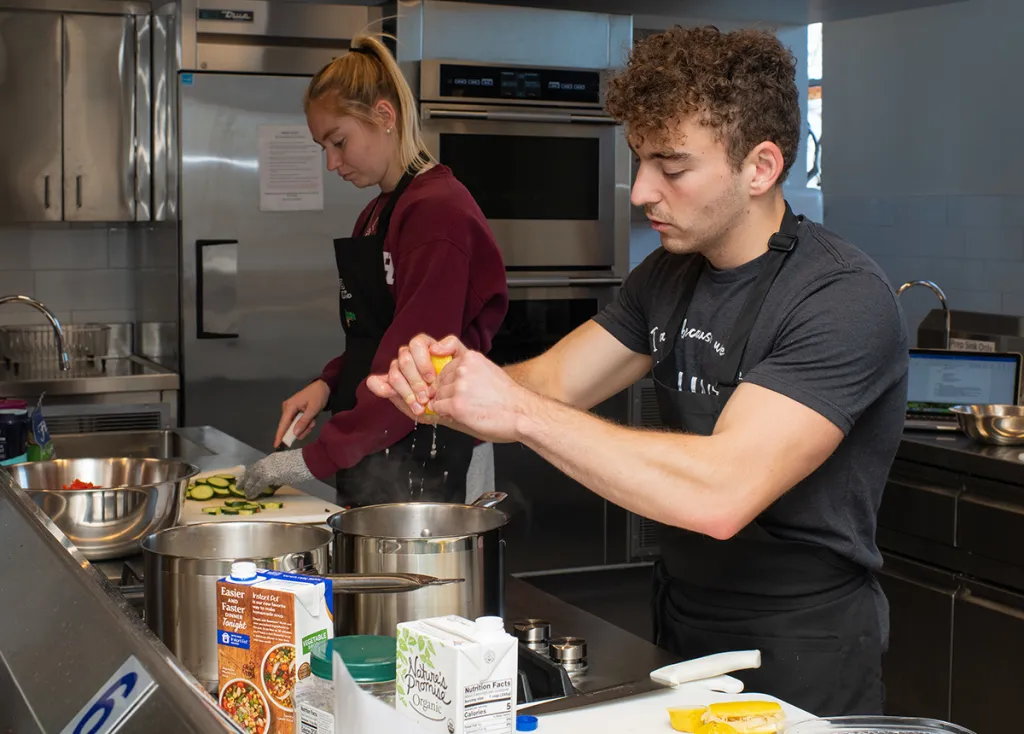 A nutrition student squeezes lemon into a pot in a large kitchen