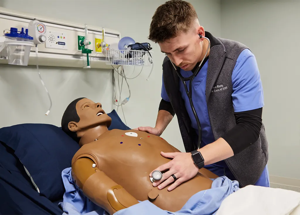 A physician assistant student listens to cardiac sounds on a patient simulator