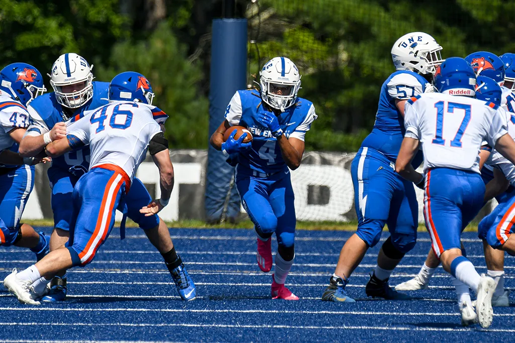 U N E football players during a game on the blue field