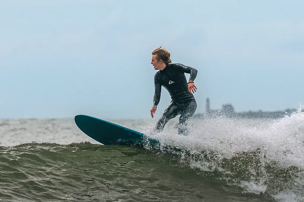 A student in a wetsuit catching a wave on a surfboard