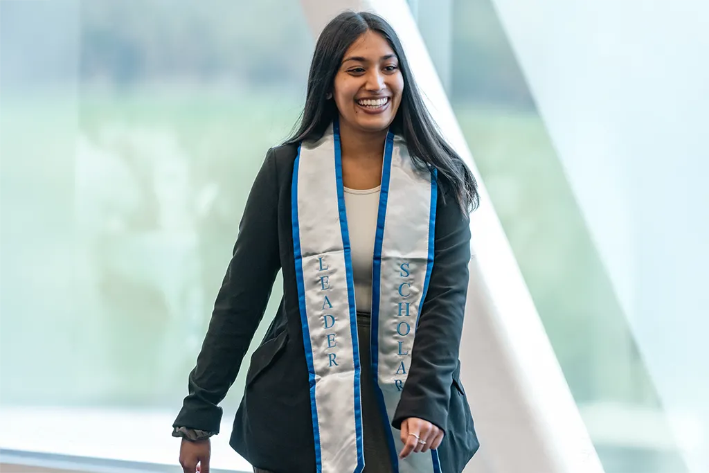 A U N E student wearing a sash that says "Leader" on one end and "Scholar" on the other