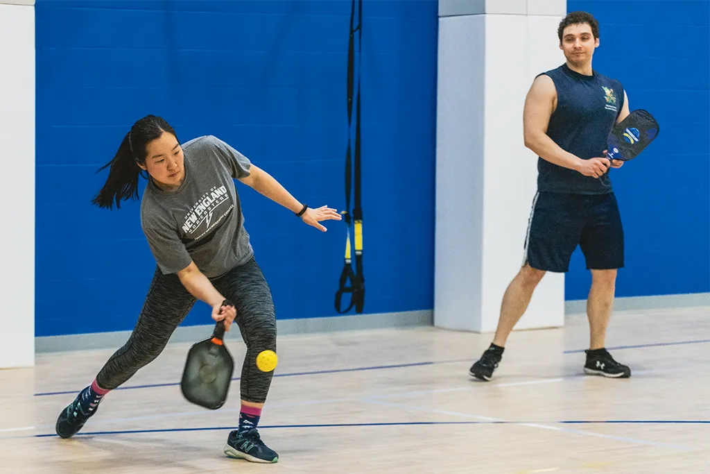 Two students play pickleball in a U N E gym