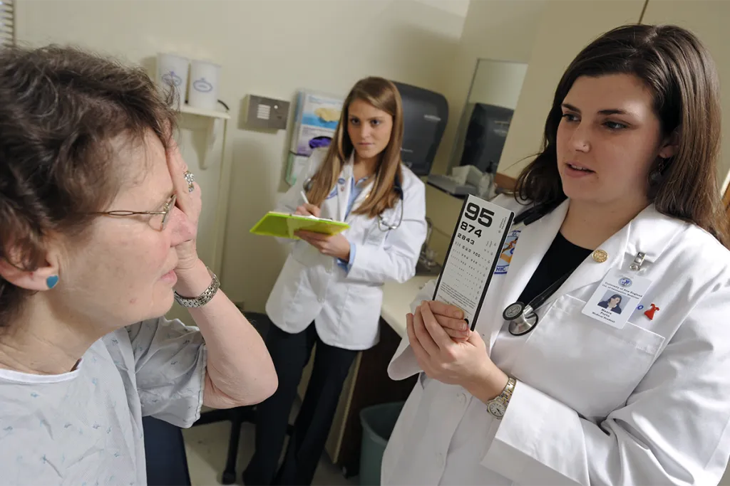 Two C O M students test a geriatric patient's eyesight in an examination room