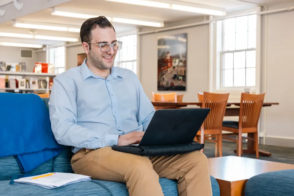 A student sitting in a library types on a laptop on their lap