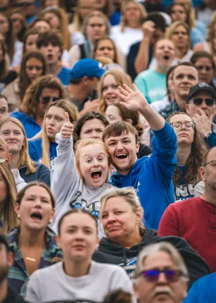 Two fans wave to the camera from the stands