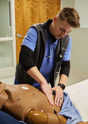 A P A student presses on a patient simulator's stomach during a lab