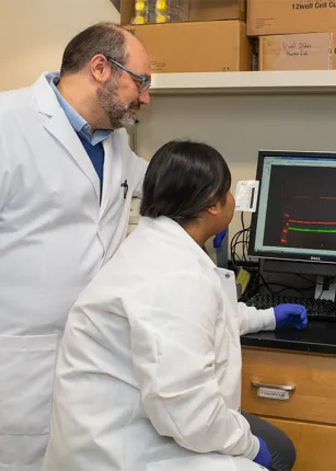 Harry Filippakis, on the left, in a while coat look at a computer screen with two graduate students in lab coats