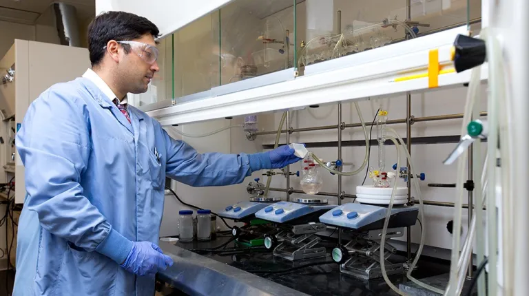 a pharmacy student wearing scrubs and safety goggles works in the lab