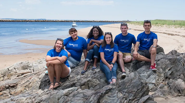 Group of U N E students sitting on a rock at the beach