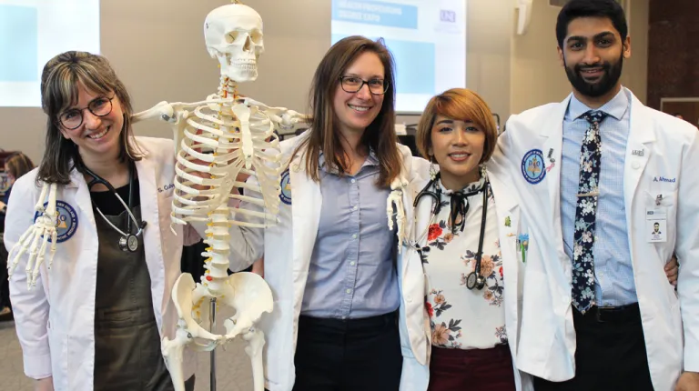 Four U N E osteopathic medicine students pose with an educational skeleton