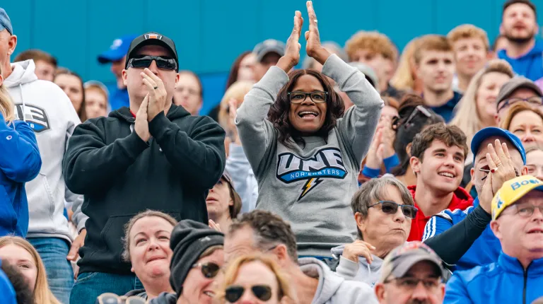 A woman in a UNE sweatshirt claps for the football team