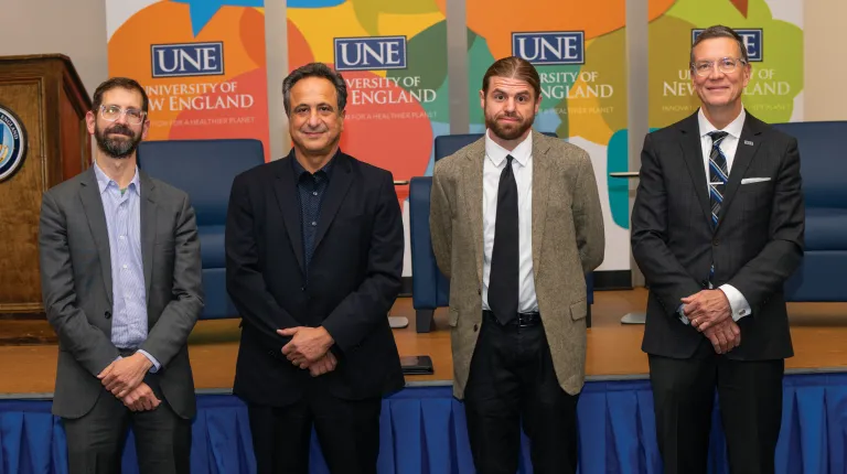 President Herbert and Anouar Majid stand with two speakers in front of banners for the U N E President's Forum