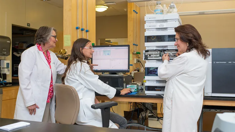 Karen Houseknecht points at a coputer screen while a UNE student in a chair looks over to another researcher 