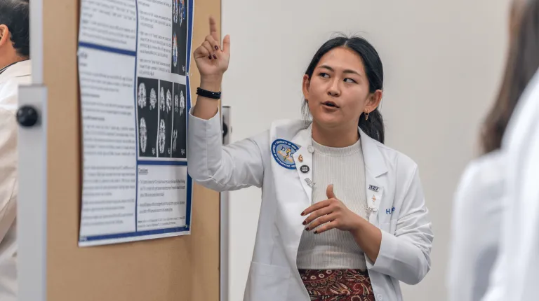 A medical student presents a research poster to a group of people