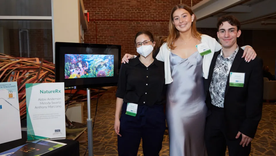 Three U N E students standing by their project at the 2022 Innovation Showcase