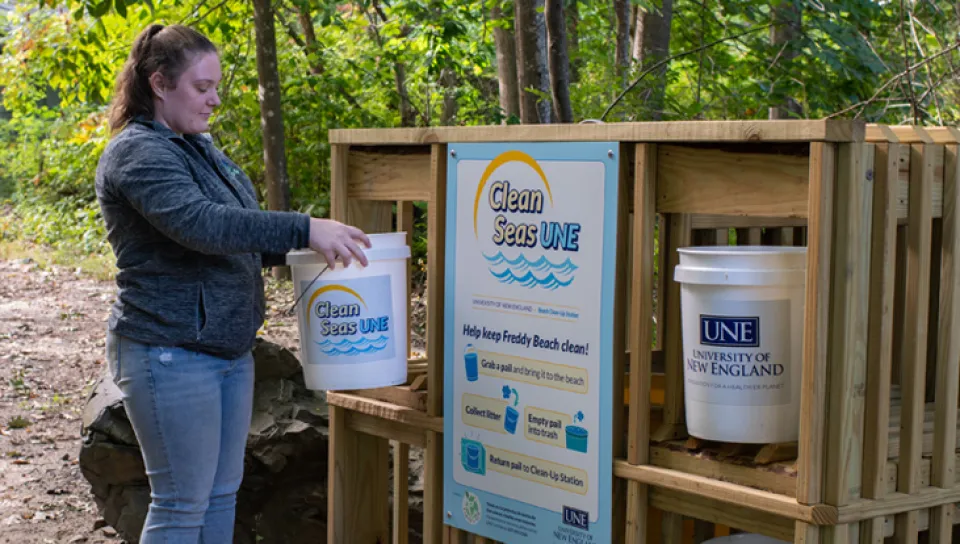 A U N E student dropping off a bucket at the Clean Seas U N E area