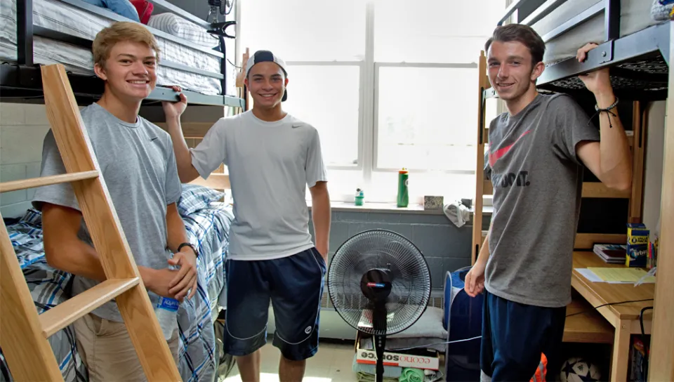 Three students standing in their dorm room