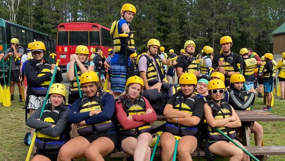 A group of U N E students wearing helmets, life vests, and holding paddles