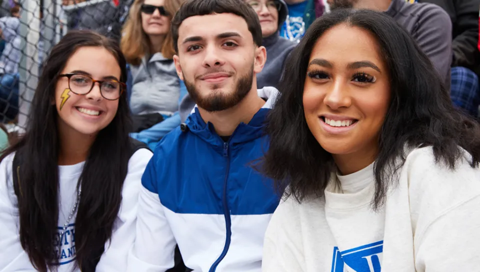 Three U N E students at a U N E football game