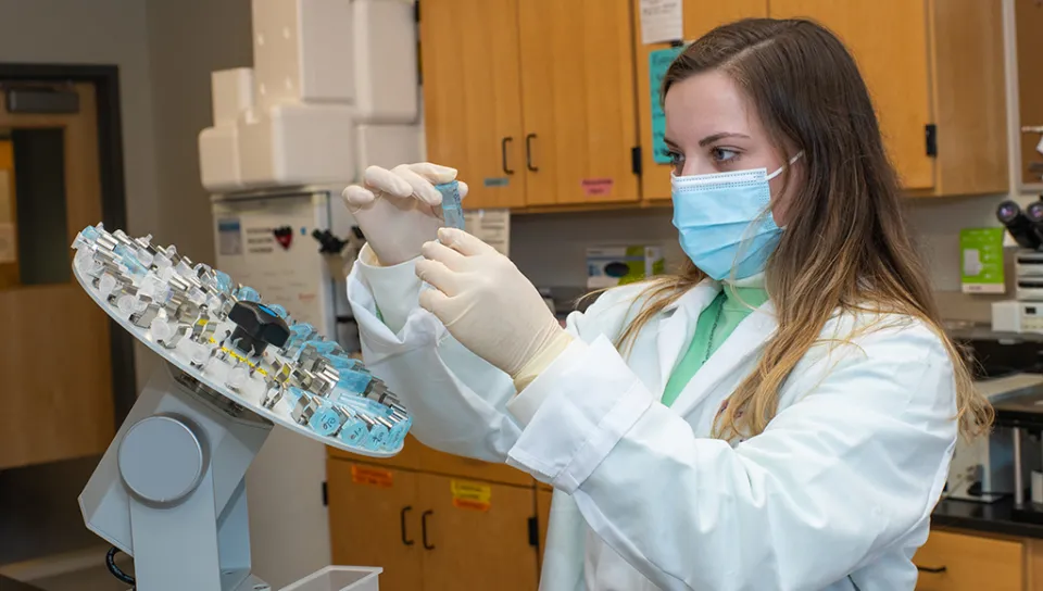 A student in a white lab coat and mask reviewing slides