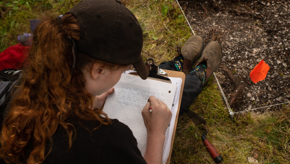 A student sitting on grass is writing notes