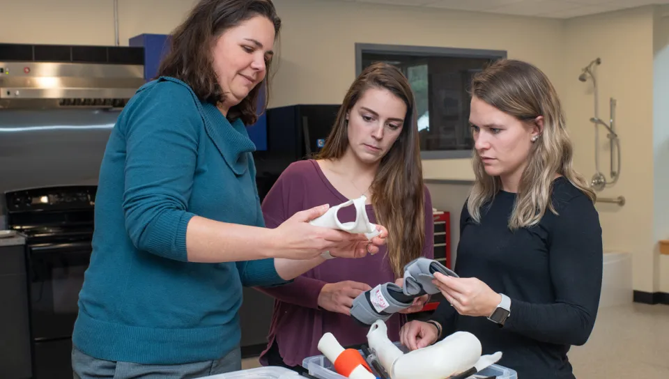 Three Occupational Therapy students standing together looking at various wrist braces