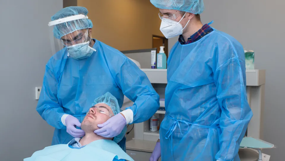 A physician assistant student assists a dental medicine student in giving a patient an exam as part of interprofessional education