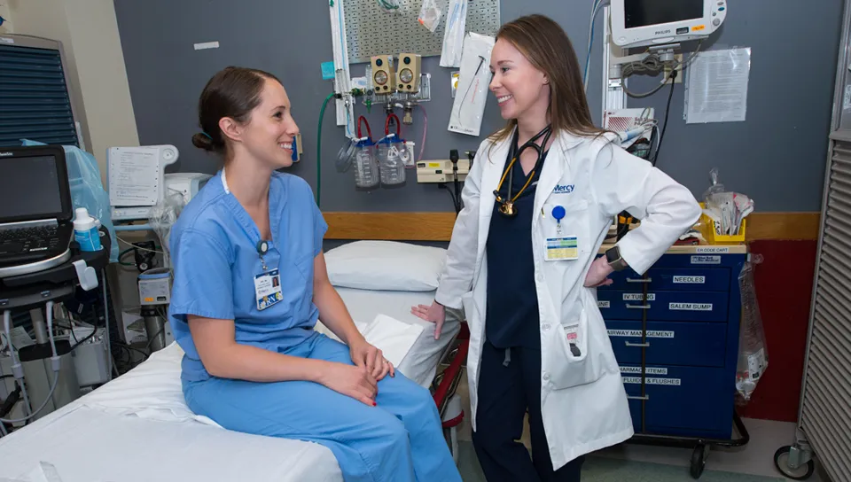 U N E Physician Assistant student in a white coat talks to a patient in a hospital room