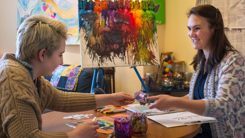 A social work student sits with a client as they paint