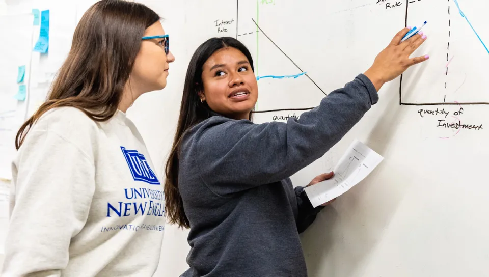 A U N E student points to a graph on a white board