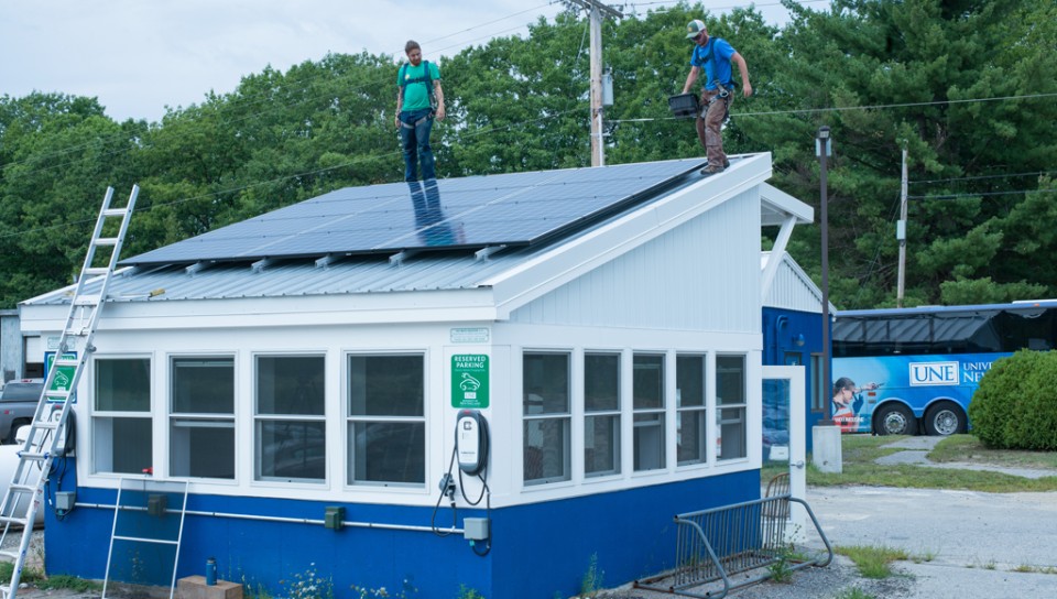 Two workers install solar panels on top of the Bishop Street Lot security building