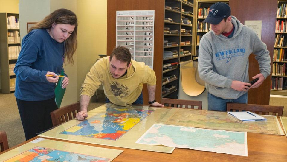 A group of students look at old maps of the United States laid out on a wooden table