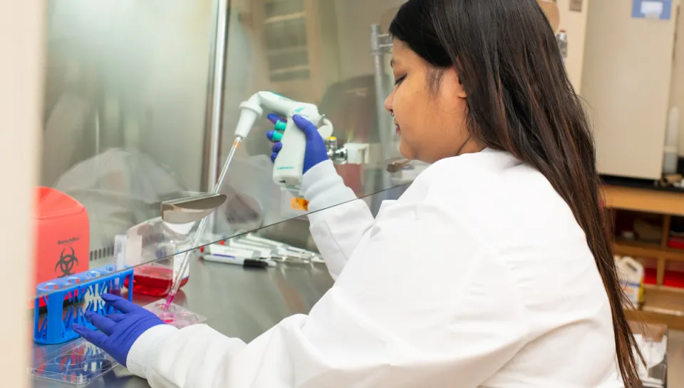 A student in a white lab coat prepares liquids into a tube