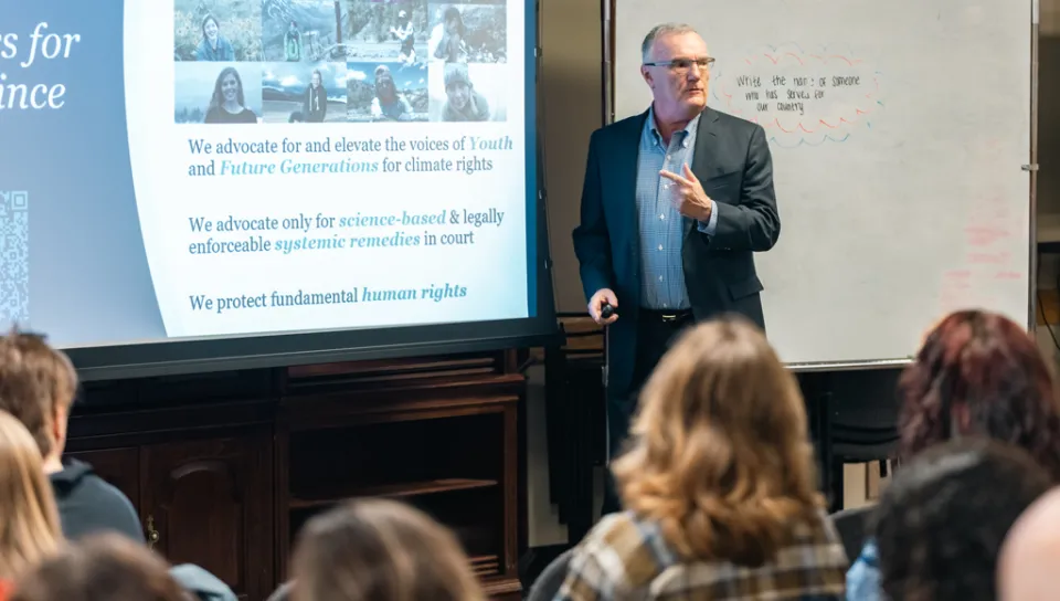 A lecturer standing in front of a presentation speaks to a group of students