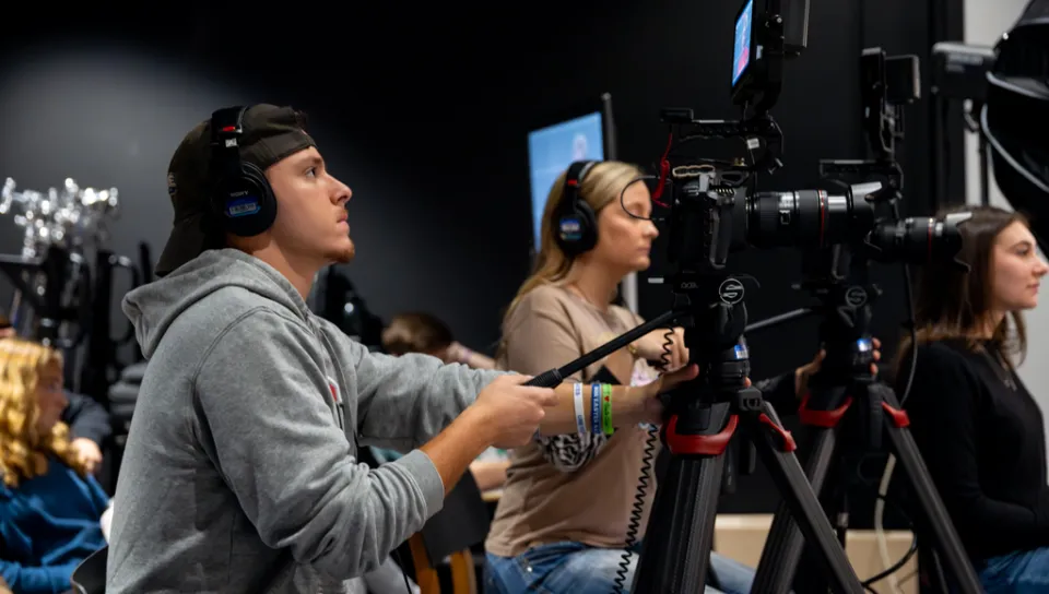 A student runs a video camera during a mock interview