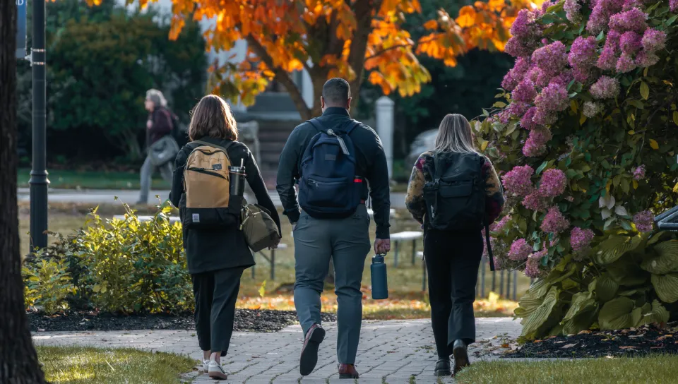 Three students walk across the Portland Campus quad during autumn