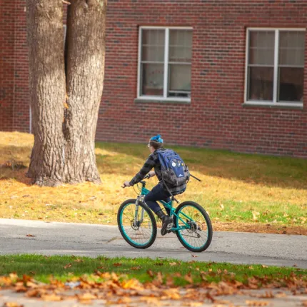 A student riding a bike on a paved path on the Biddeford Campus