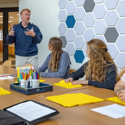 A professor talks to two students during a class