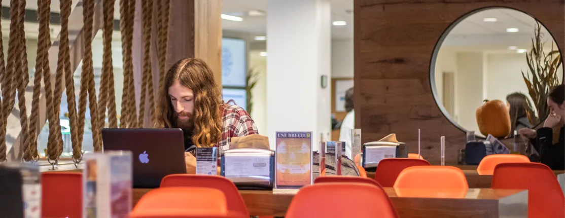 A student works on their laptop in the Commons dining room