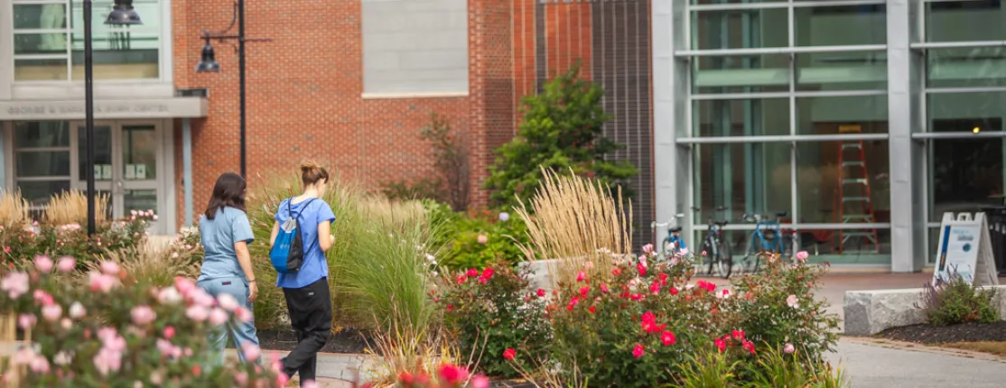 Two students walking towards a large brick building surrounded by a garden