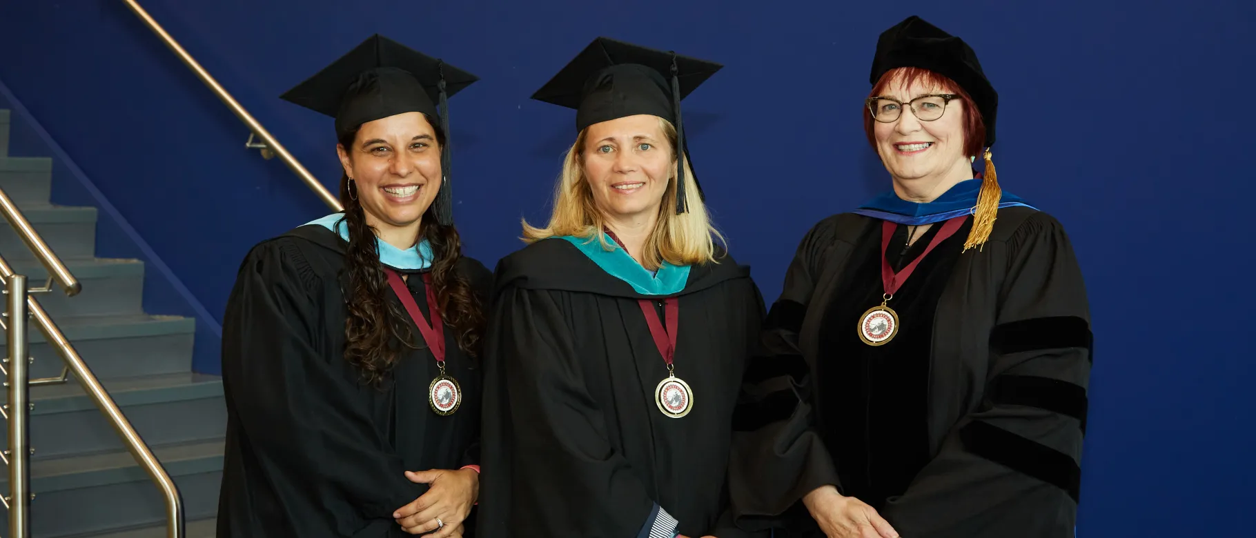 Julia Sleeper-Whiting, Hannah Pingree, and Lise Pelletier pose for a photo in academic regalia 