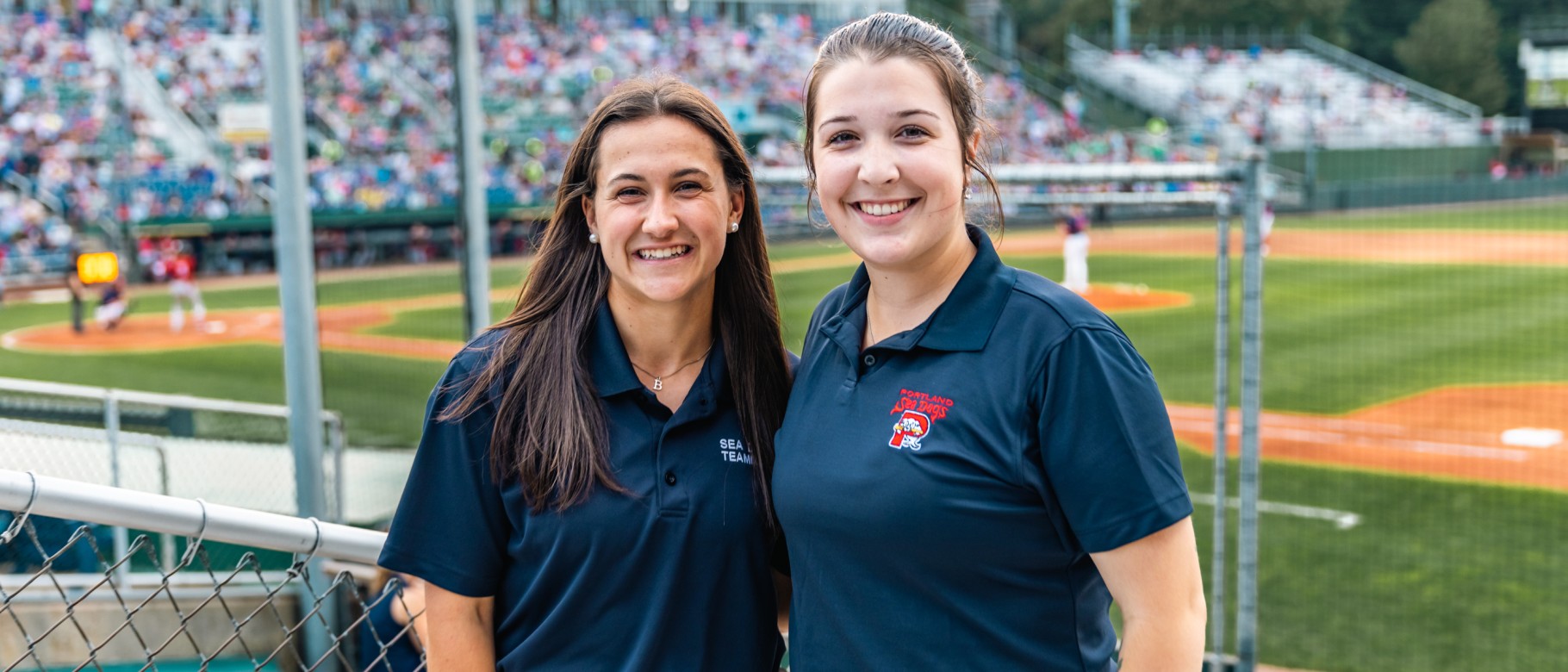 Two UNE business students pose in front of the baseball diamond at Portland's Hadlock Field