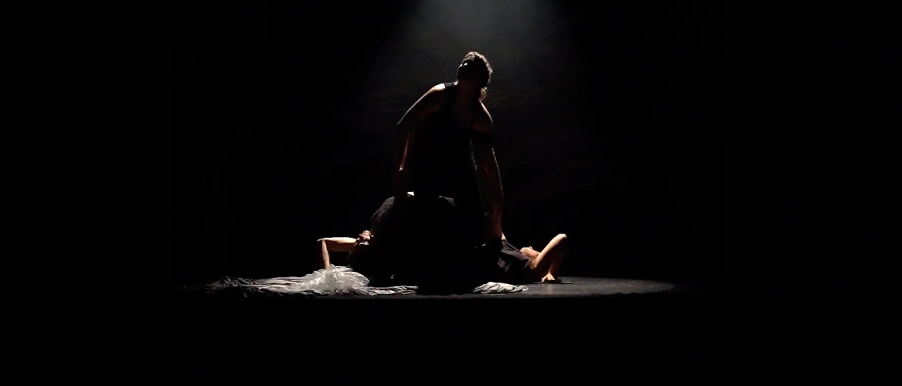 Dancers move around a dark stage twirling fabric