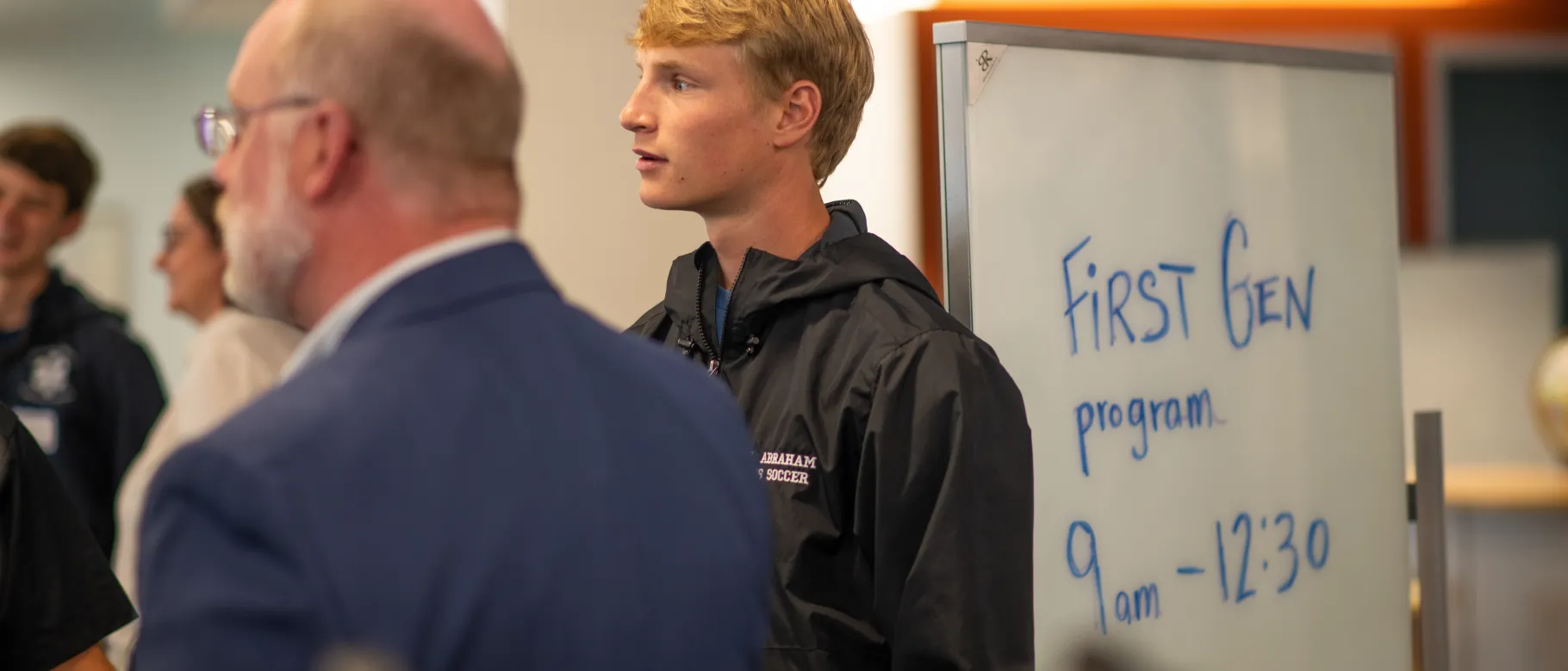 Student stands in front of sign for first-gen orientation.