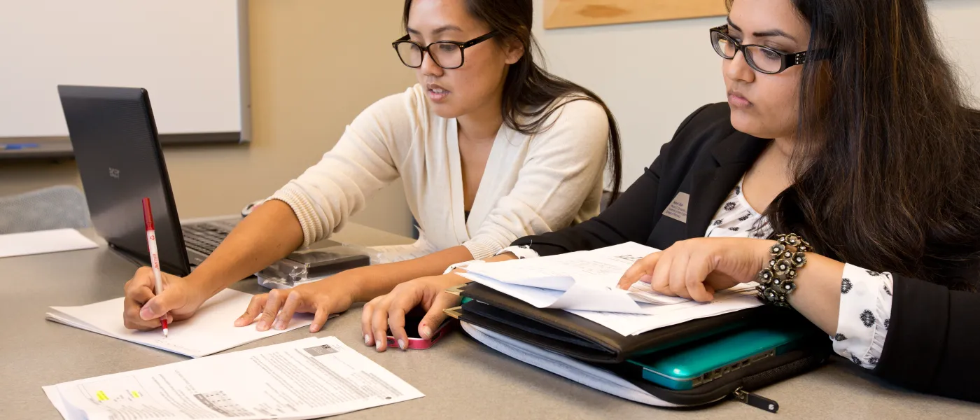 Two female students study at a long table 