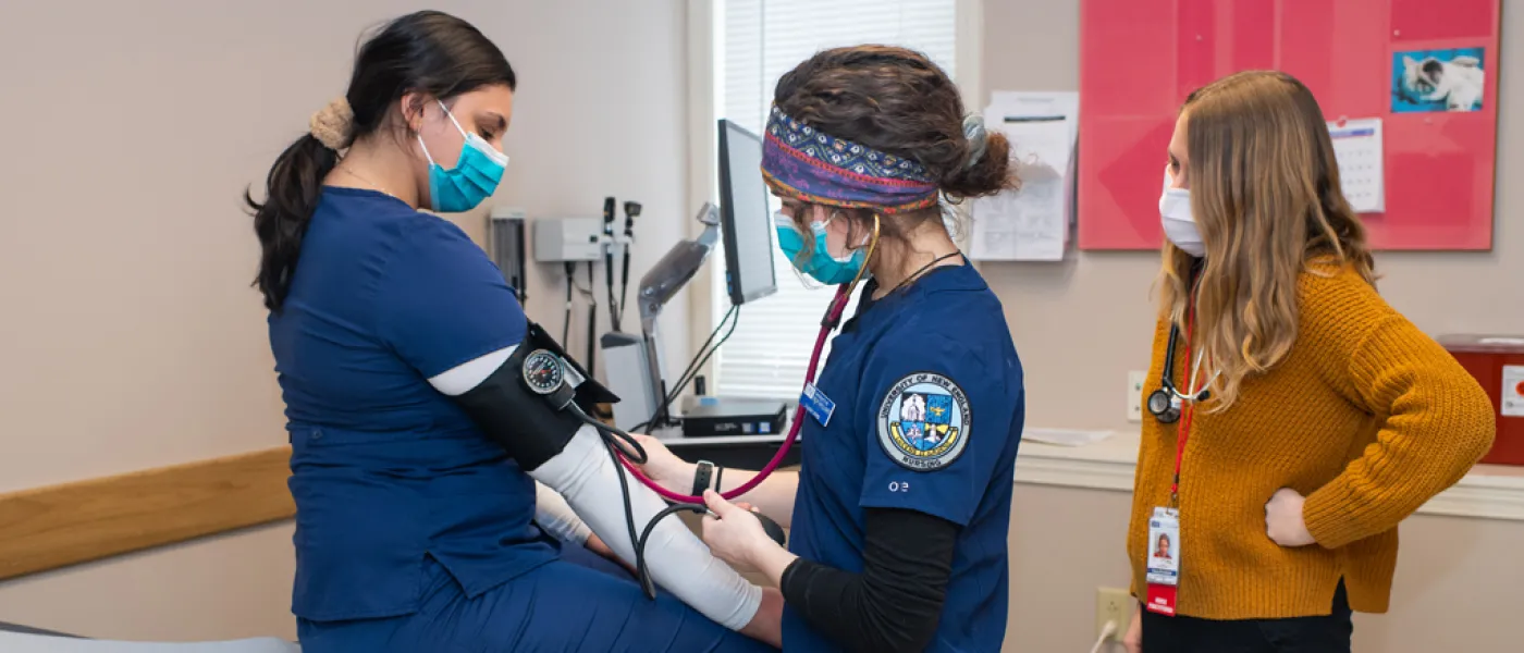 Two U N E health professions students perform a blood pressure exam on a third student in a hospital room