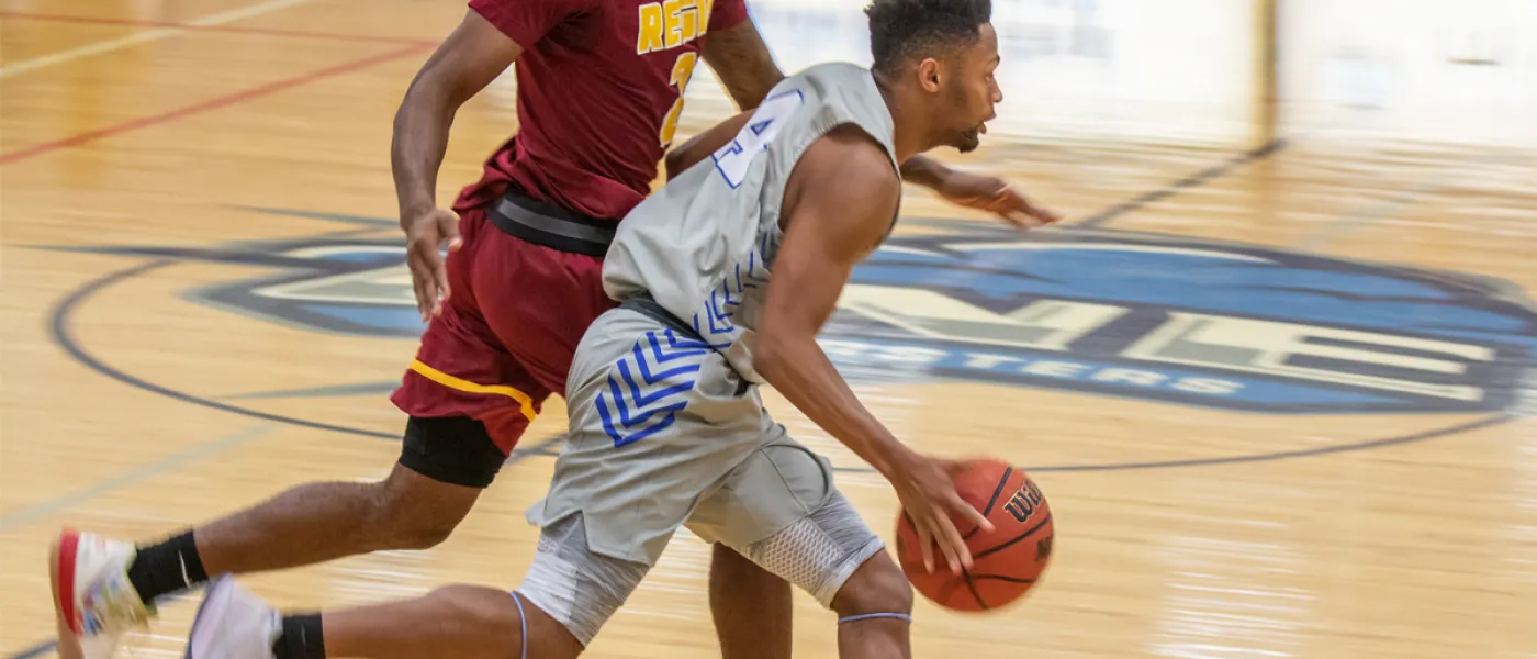 A U N E basketball player dribbles the ball across the U N E court during a game