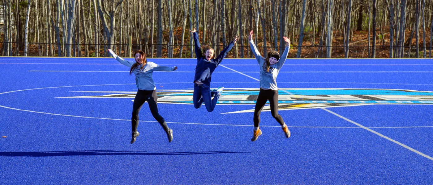 Three students jumping off the Blue Bolt Field on the Biddeford Campus