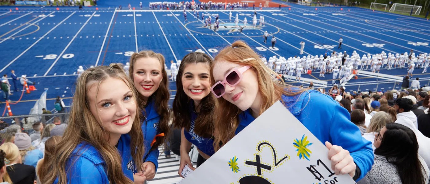 Four students cheering on the U N E football team at a home game