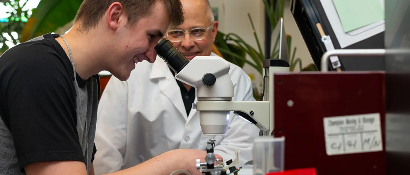 A professor helps as a student peers into a microscope